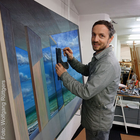 Maleren Tobias Stutz smiler til kameraet, mens han arbejder på et billede i sit atelier.