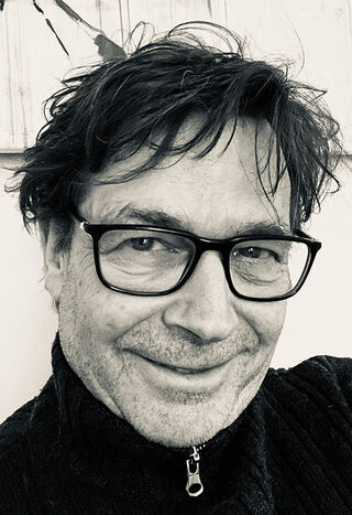 Schwarz-Weiß-Porträt des Malers Axel Kostorz mit Brille und dunklem Strickpullover.