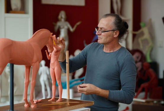 Le sculpteur SIME travaille avec application sur une nouvelle sculpture en argile dans son atelier.