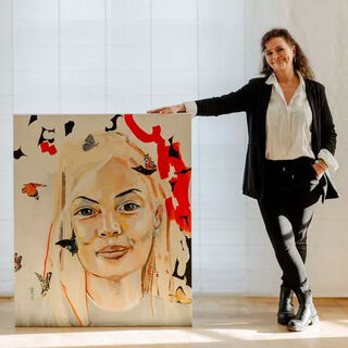 The painter Petra Girschewski stands smiling next to a large portrait.