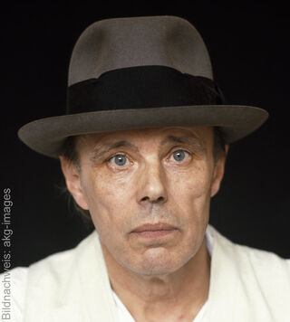 Ritratto dell’artista tedesco Joseph Beuys con il suo caratteristico cappello di feltro grigio su uno sfondo scuro.