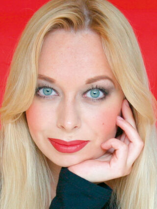 Die Malerin Ekaterina Moré blickt mit blonden Haaren, roten Lippen und aufgestütztem Kinn in die Kamera.