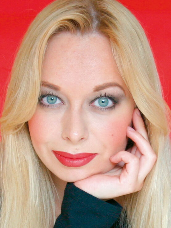 Die Malerin Ekaterina Moré blickt mit blonden Haaren, roten Lippen und aufgestütztem Kinn in die Kamera.
