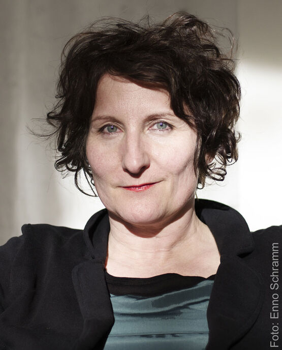 Porträtaufnahme der Künstlerin Sabine Wild mit dunklen, lockigen Haaren, die direkt in die Kamera blickt.