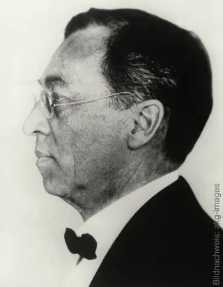 Photographie historique en noir et blanc représentant l'artiste et peintre russe de l'expressionnisme abstrait Wassily Kandinsky, vu de profil, portant des lunettes et un nœud papillon.