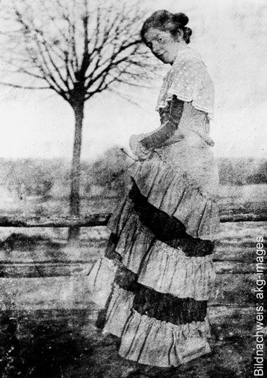 Historisk svartvit fotografi av konstnären Paula Modersohn-Becker utomhus, klädd i en lång klänning med trappstegsformad kjol.