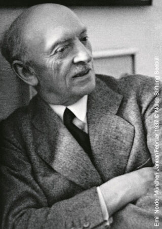 Historische Schwarz-Weiß-Fotografie des expressionistischen Malers Emil Nolde im Tweed-Sakko mit verschränkten Armen.
