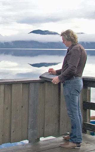 Maleren Ansgar Skiba står på en træbro ved en sø og tegner et landskab.