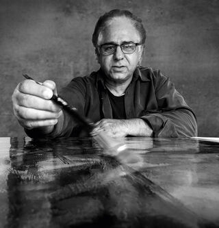 Schwarz-Weiß-Fotografie des Künstlers und Malers Asghar Keyhanian mit Brille bei der Arbeit mit einem Pinsel an einem Gemälde.