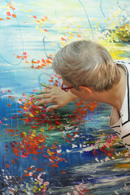 L'artista Ute Bivona stende con le dita della pittura rossa su un grande dipinto paesaggistico dai toni blu e colorati.