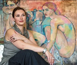 Den russiske kunstner og maler Marina Krasnitskaya sidder smilende foran et af sine storformatsmalerier med kvindeakt.