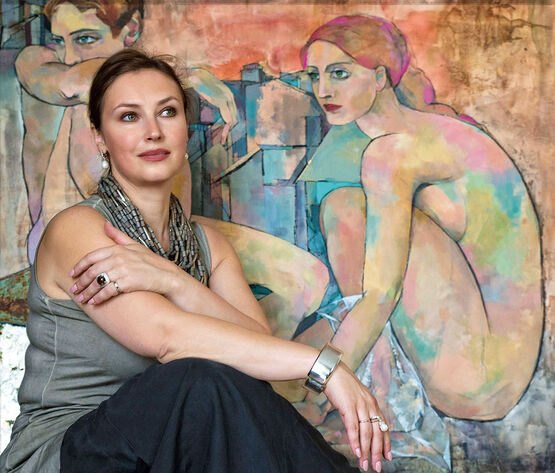 Ruská umělkyně a malířka Marina Krasnitskaya sedí s úsměvem před jedním ze svých velkoformátových obrazů s ženskými akty.