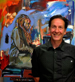 Der deutsche Maler Jürgen Born lächelnd vor einem seiner farbenfrohen, expressionistischen Gemälde