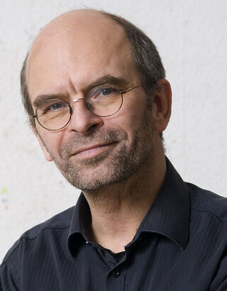 Porträt des Künstlers Jens Wohlrab mit Brille und dunklem Hemd, der leicht lächelnd in die Kamera blickt.