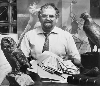 Bildhauer Kurt Arentz sitzt mit Dokumenten am Tisch, umgeben von seinen Bronzeskulpturen einer Eule und eines Falken.