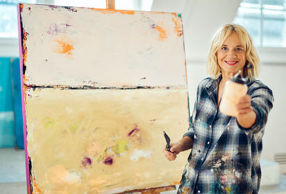 Kunstneren Jana Dettmer står smilende i sit atelier ved siden af et stort abstrakt lærred.