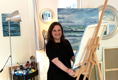 Malerin Sandra Gebhardt-Höpfner sitzt lächelnd an der Staffelei im Atelier.