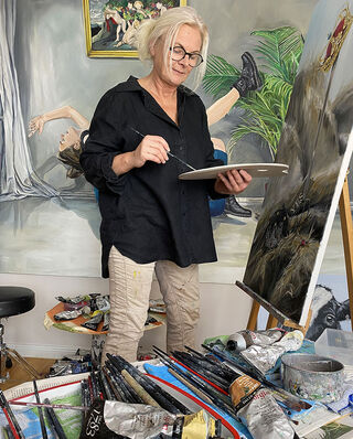 Die deutsche Künstlerin und Malerin Birgit Horn mit Brille und Mischpalette beim Malen an einer Staffelei in ihrem Atelier.