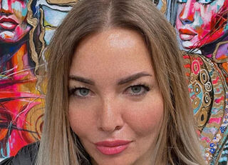 Portret artystki i malarki Lany Frey przed dwoma jej barwnymi, ekspresjonistycznymi obrazami przedstawiającymi portrety kobiet.