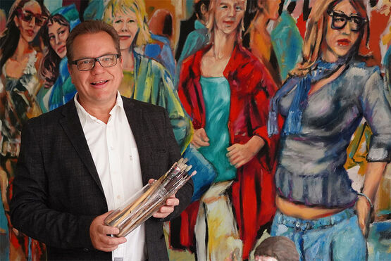 Německý umělec, malíř a sochař Klaus Dobrunz se usmívá se sklenicí plnou štětců před jedním ze svých velkých, barevných obrazů.