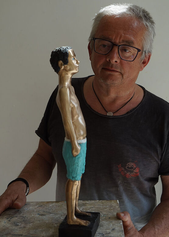 L’artista e scultore tedesco Peter Hermann, con gli occhiali, osserva concentrato la sua scultura raffigurante un ragazzo in costume da bagno.