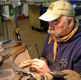 L'artista Klaus Börner lavora con grande concentrazione alla realizzazione di una piccola scultura nel suo laboratorio di oreficeria, utilizzando una sega per metalli di precisione.