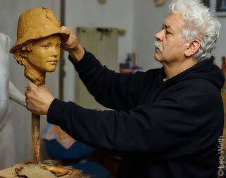 Lo scultore tedesco Leo Wirth lavora concentrato nel suo studio a un busto in argilla con un cappello.