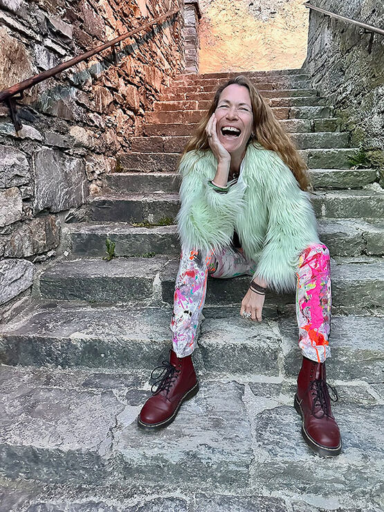 Anna Schellberg, peintre originaire de Hambourg, est assise sur un escalier en pierre et rit.