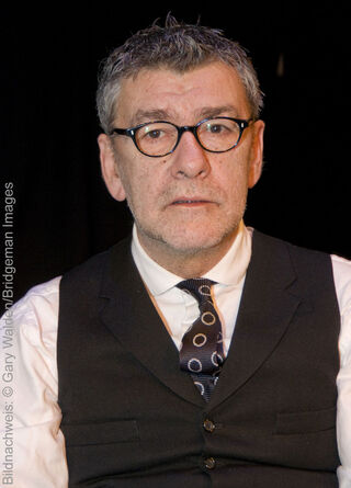 Der schottische Maler Jack Vettriano blickt mit Brille, Weste und gemusterter Krawatte direkt in die Kamera.