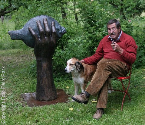 Německý spisovatel, umělec, malíř a sochař Günter Grass sedí v zahradě s dýmkou na židli vedle psa a se svou sochou „Butt“ v ruce.