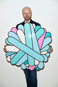 L'artista Daniel Engelberg tiene in mano un'opera scultorea circolare e colorata realizzata con pannelli in MDF.