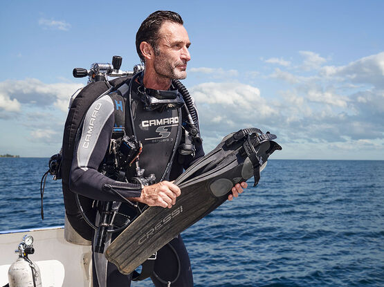L'artiste et photographe autrichien Andreas Franke, en tenue de plongée complète et muni de palmes, sur un bateau en pleine mer.