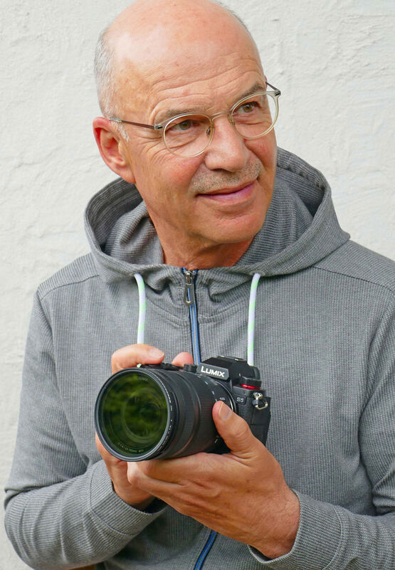 Portrét fotografa Gottfrieda Römera s brýlemi, který drží v rukou fotoaparát Lumix.