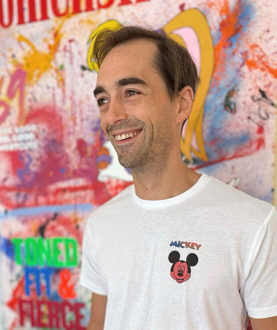 Umělec pop-artu TED se usmívá z profilu na pozadí jednoho ze svých barevných a živých uměleckých děl.