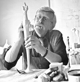 Een zwart-witfoto van de kunstenaar Paul Wunderlich, die geconcentreerd aan een sculptuur werkt.